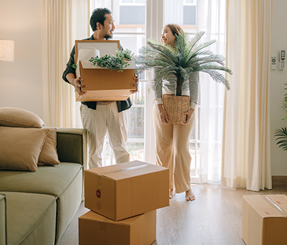 Man and woman carry moving boxes and a plant into their new place