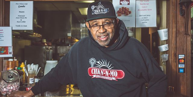 Owner of Chkn-N-Mo standing in his restaurant, smiling