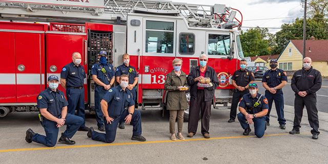 Firefighters posing with man and woman who are holding cookies