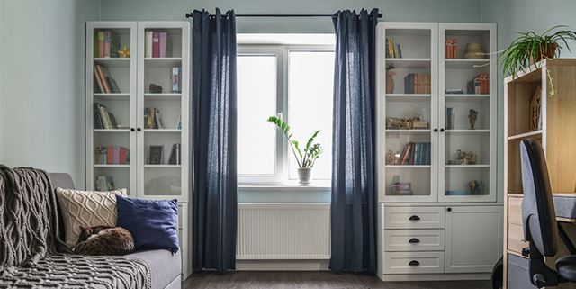Room with white bookcases, grey sofa, blue curtains