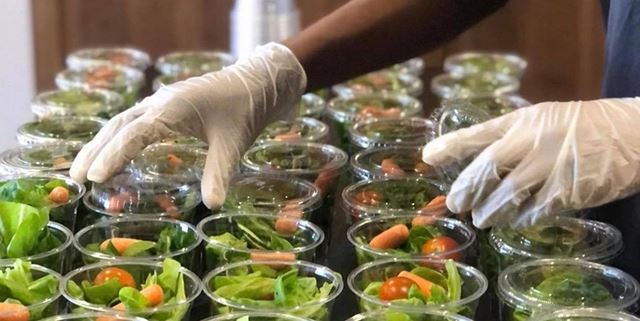 Closeup of gloved hands putting lids on cups of salad