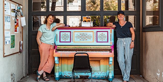 Two women standing by a colorful piano