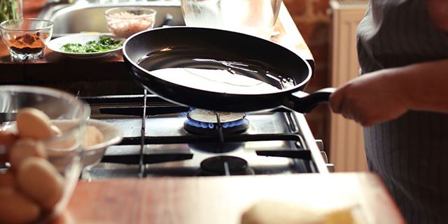 Closeup of a woman cooking on her natural gas stove - she is heating up a pan to make eggs