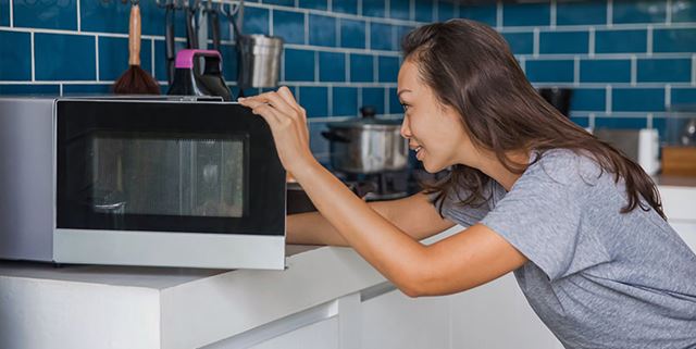 Woman opens microwave to check on reheated meal