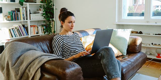 Woman sitting on sofa at home, working on her laptop