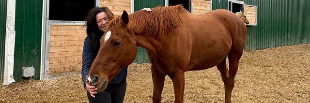 Woman smiles and pets a brown horse outdoors.