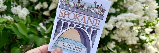 A paper version of a This is Spokane, A Civic Guide for Neighbors held in a person's hand in front of some flowering trees.