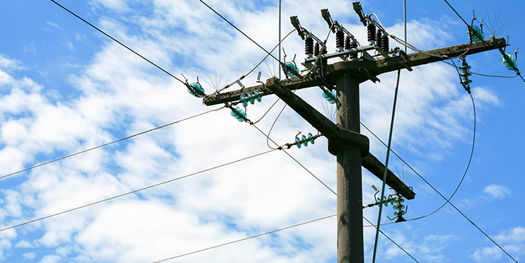 Wooden utility pole in front of blue sky with clouds