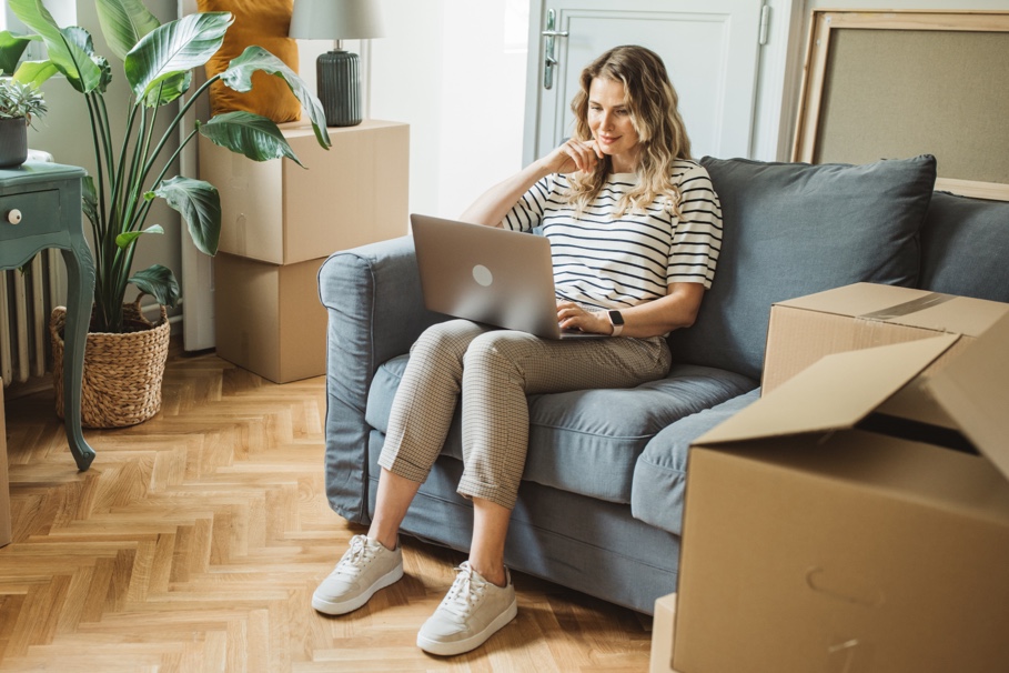 Woman reading the Porch website on a laptop with moving boxes scattered around her living room