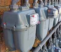 Natural gas meters in a row outside against the wall.