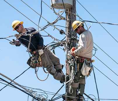Two linemen working on a power pole with a blue sky