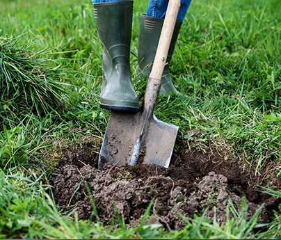 Person wearing boots and digging in their yard with a shovel.