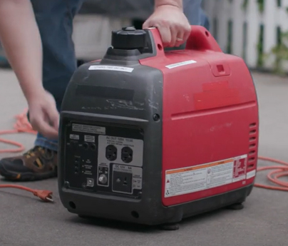 Red and black gas generator sitting outside, a man is bending down to start it.