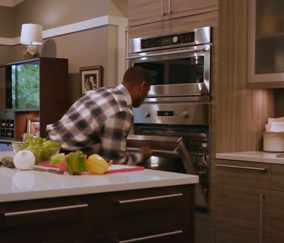 Man opens oven to smell inside of it, there are vegetables on the kitchen counter as he is in the middle of preparing a meal.